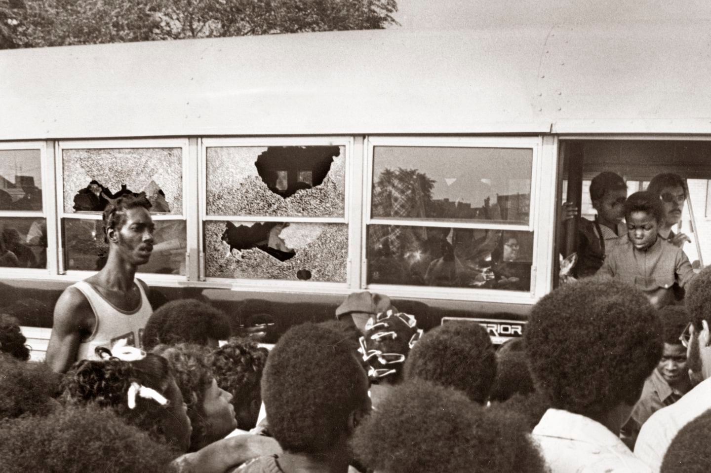 A crowd watches as a bus carrying students returns to Columbia Point with broken windows on Sept. 12, 1974, the first day of school under the new busing system put in place to desegregate Boston Public Schools.